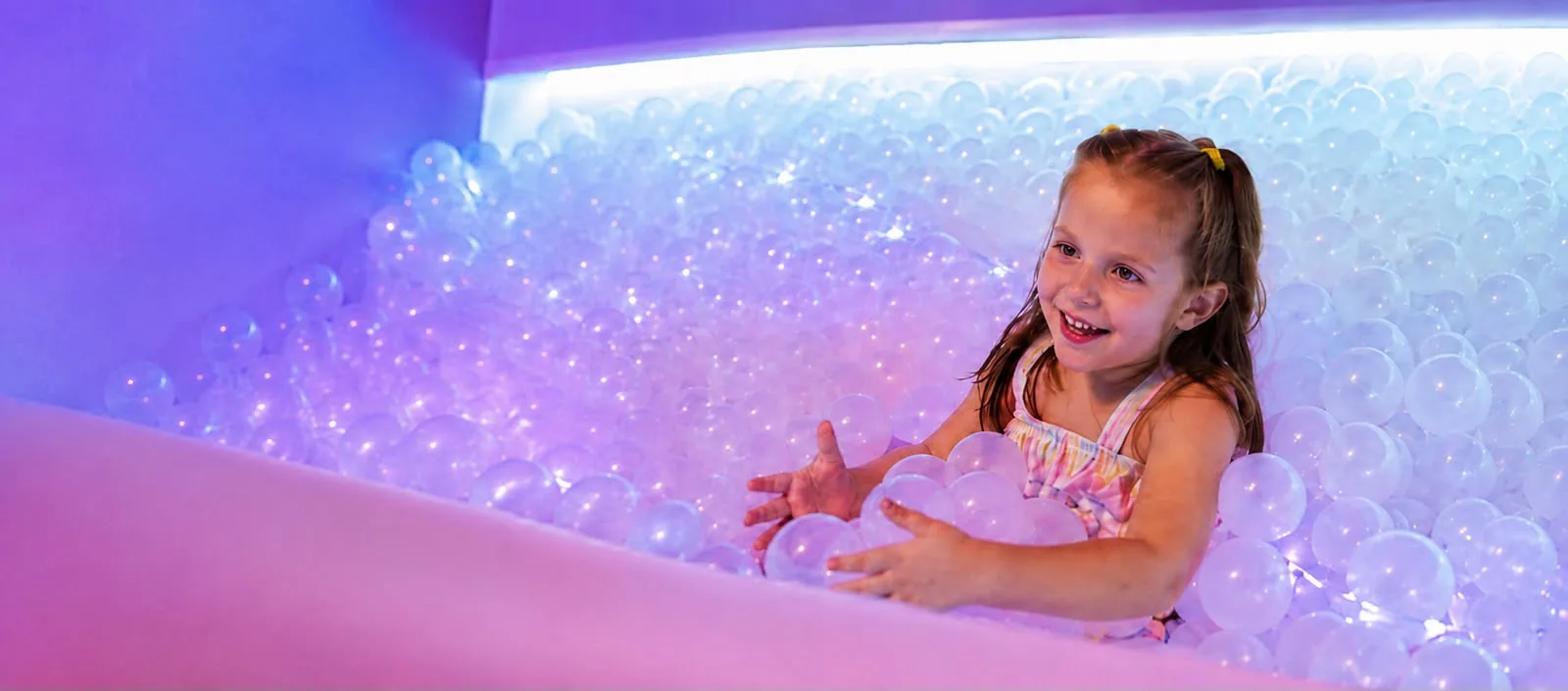 Niña sonriendo en la alberca de pelotas iluminada de la sala multisensorial